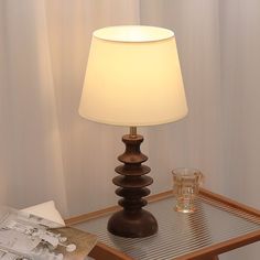 a lamp sitting on top of a wooden table next to a glass filled with water