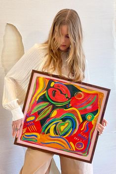 a woman is holding up a colorful painting