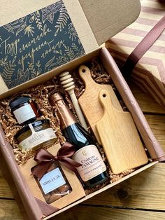 an open gift box containing two bottles of wine, cheese and jams with a wooden cutting board