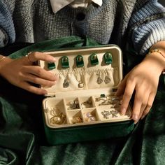 a woman is holding an open green case with jewelry in it