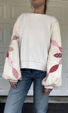 a woman standing in front of a garage door wearing jeans and a sweater with fish appliques