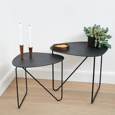 two black tables with candles on them in front of a white wall