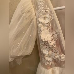 the back of a wedding dress with flowers on it and sheer fabric hanging up against a wall