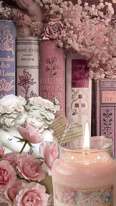 there is a candle that is next to some books with flowers on the shelf in front of it