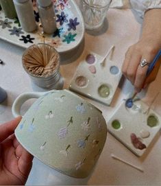 a person is painting with paintbrushes on a white cup and other items in the background