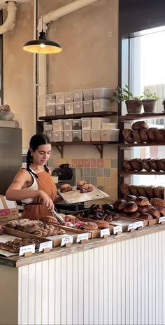 a woman standing behind a counter filled with donuts