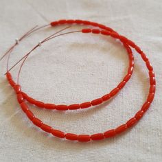 two red beaded necklaces sitting on top of a white cloth