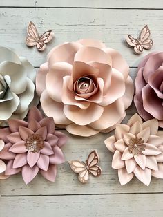 paper flowers and butterflies are arranged on a white wooden surface, with one large pink flower in the center