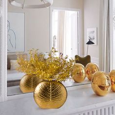 a white mantle topped with gold vases filled with flowers next to a large mirror