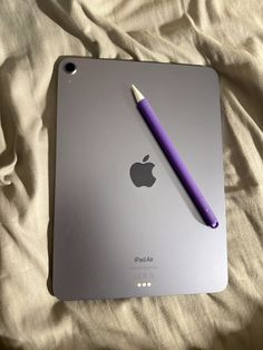 an apple ipad with a purple pen sitting on it's back cover in the bed