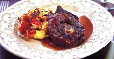 a white plate topped with meat and gravy on top of a wooden table