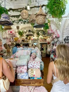 two women are looking at fabrics in a store with hanging plants and baskets on the ceiling