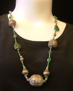 a woman wearing a black shirt and green beaded necklace on a mannequin