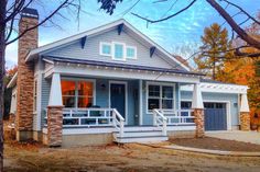 a small blue house with white trim and brick pillars on the front porch is surrounded by trees