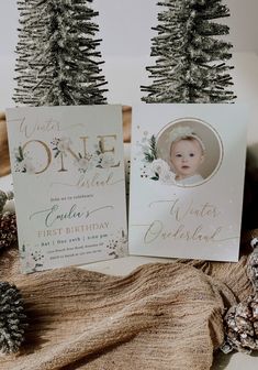 two christmas cards sitting on top of a table next to pine cones and fir trees