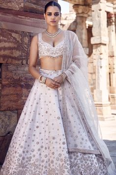 Introducing the ekru royal nandi lehenga, crafted from sumptuous ivory raw silk, redefining luxury with every stitch. This masterpiece showcases the exquisite anmol dori work and intricate hand embroidery, embellished with pearls, mirrors, and sequins, reflecting dedication to traditional Indian craftsmanship. The detailed floral and paisley patterns intertwine seamlessly with our unconventional yet signature v-wing design, creating a captivating fusion of heritage and innovation. Raw Silk Embroidery, Dori Work, Wing Design, Pearl Embroidery, Ivory Blouse, Wings Design, Net Dupatta, Silk Embroidery, Traditional Indian