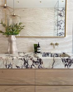 a bathroom vanity with marble counter top and gold framed mirror above it, along with a white vase filled with flowers