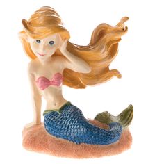 a little mermaid figurine sitting on top of a sandy beach with her hair blowing in the wind