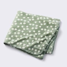 a green and white flowered blanket folded on top of a gray surface with small white flowers all over it