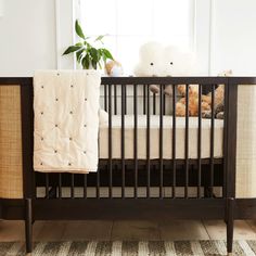 two teddy bears sitting on top of a crib in front of a potted plant