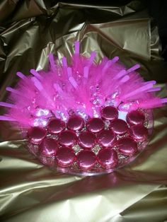 a bowl filled with pink candles on top of a shiny foil covered table cloth,