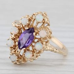 Gemstone Information: - Natural Amethyst - Carats - 0.50ct  Cut - Marquise Brilliant Color - Purple - Natural Opals - Size - 2.2 - 2.4 mm Cut - Round Cabochon Color - White with multicolor flecks Metal: 10k Yellow Gold  Weight: 3.5 Grams  Stamps: 10k Face Height: 19 mm  Rise Above Finger: 7.7 mm Band / Shank Width: 1.7 mm This ring is a size 7 1/4, but it can be resized down 2 sizes for a $20 fee or up 3 sizes for a $25 fee. If you would like your ring resized, please select the appropriate fee from the listing below in order to pay the sizing fee: https://www.etsy.com/listing/781388346/ring-sizing-service-fee Each piece is thoroughly examined and refinished as needed by our professional jewelers, graded by our in-house GIA (Gemological Institute of America) Graduate Gemologist, and inspec Heirloom Amethyst Jewelry As Birthstone, Estate Style 14k Gold Oval Jewelry, Heirloom 14k Stamped Amethyst Jewelry, Marquise Amethyst Jewelry With Accent Stones, Antique 14k Gold Cluster Jewelry, Estate Style 14k Yellow Gold Jewelry, Antique Multi-stone Cluster Jewelry, Estate Oval Jewelry For Gifts, Collectible Yellow Gold Jewelry With Accent Stones