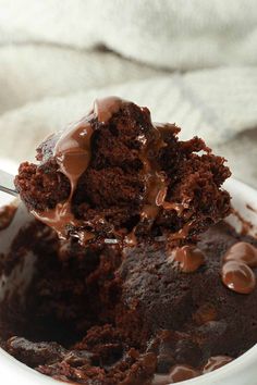 a spoon full of chocolate ice cream on top of a white bowl filled with cake