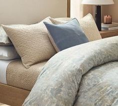 a bed with blue and white comforter next to a night stand in a bedroom