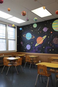 an empty classroom with desks and chairs in front of a solar system wall mural