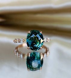 two rings with blue and green stones on them sitting on a white cloth covered surface