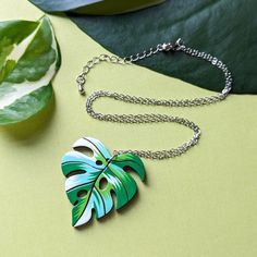 "Inspired by the Albo Borsigiana variegated monstera deliciosa, this unique heart-shaped leaf necklace will add a luxurious botanical flair to your wardrobe or bring a personal hand-made touch as a gift to a loved one. This original design is hand painted on cherry wood with a beautiful patchwork palette of white and green. The subtle heart shape of the leaf adds even more character to an already unique necklace. Lightweight and durable, this necklace is sure to capture the heart of any plant lo Trendy Leaf-shaped Jewelry Gift, Trendy Green Leaf-shaped Jewelry, Handmade Tropical Green Jewelry, Multicolor Leaf-shaped Jewelry Gift, Handmade Green Leaf Necklace, Multicolor Leaf Shaped Jewelry For Gifts, Tropical Style Multicolor Jewelry As Gift, Unique Green Heart-shaped Necklace, Green Leaf-shaped Botanical Jewelry