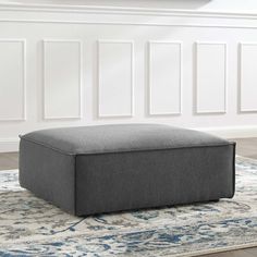 a gray ottoman sitting on top of a rug in front of a white wall and floor