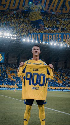 a soccer player holding up a yellow jersey in front of a stadium full of fans