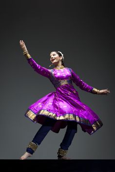 a woman in a purple and gold dress is dancing with her arms out to the side