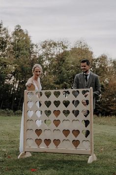 a man and woman standing next to a giant wooden board with heart cutouts on it