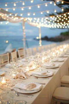 a long table is set up with white plates and place settings for dinner at the beach