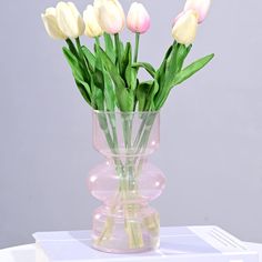 a vase filled with white and pink tulips on top of a table