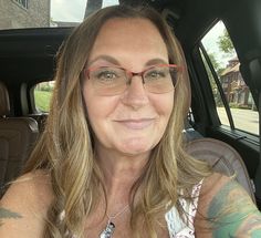 a woman wearing glasses sitting in the back seat of a car with tattoos on her arm