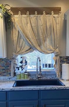 a kitchen sink under a window next to a counter top with an open curtain over it