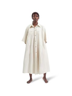 This ivory shirt dress by THIS IS US™ is designed in an oversized silhouette, enhanced by roomy pockets. It's made in Nigeria from native cotton and features a classic pointed collar, boxy sleeves, and mother-of-pearl shell buttons, offering versatility and style for every occasion. A must-have wardrobe staple, we also have the indigo version in our edit. - Pointed collar, boxy sleeves, oversized pockets, mother-of-pearl buttons, maxi length- Cotton- Crafted using locally grown cotton and natural indigo dyes sourced from the Kano dye pits in Kofar Mata, reviving Nigeria’s age-old traditions- Each piece is made to order by artisans and can take up to 3 weeks to complete- Made in Lagos, Nigeria, ships from Nigeria Oversized Button-up Dress, Oversized V-neck Shirt Dress For Daywear, Oversized Button-up Dresses For Daywear, Oversized Button-up Shirt Dress With Pockets, Oversized Cotton Knee-length Shirt Dress, African Luxury, Oversized Pockets, Natural Indigo Dye, Oversized Shirt Dress