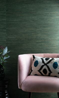 a pink chair with a black and white pillow on it in front of a green wall