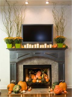 a fireplace with candles and pumpkins in front of the tv on top of it