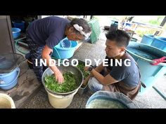 two men sitting on the ground next to buckets filled with green plants and water