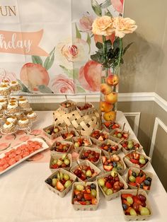 a table topped with lots of fruit and cupcakes next to a vase filled with flowers