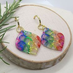 a pair of colorful earrings sitting on top of a piece of wood next to a pine branch