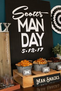 a man's day party with snacks and drinks on the table in front of a sign