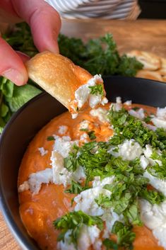 a person dipping food into a bowl with bread and parsley on the side at a restaurant