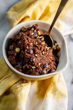 a bowl filled with chocolate and nuts on top of a yellow towel next to a spoon