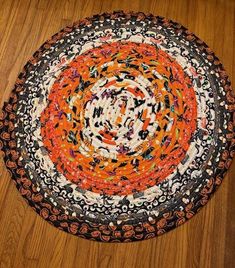 an orange, black and white circular rug on a wooden floor in the middle of a room