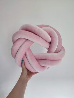 a hand holding up a pink knot made out of felt and wool yarn on a white background